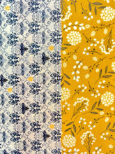 Load image into Gallery viewer, Two beeswax wraps side by side. One is black and white with honeybees, the other is a golden color. 